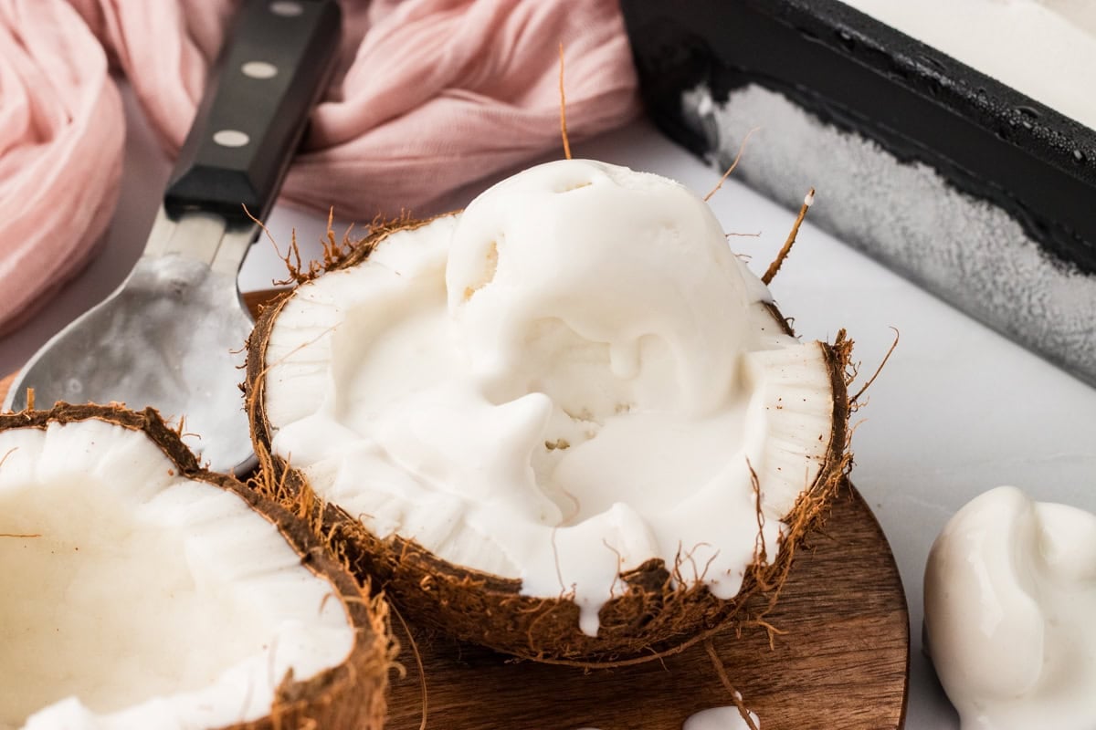 Coconut sorbet scooped into a fresh coconut shell with melted coconut cream dripping over the sides.