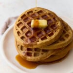 Stack of oat flour waffles topped with butter and maple syrup on a white plate.