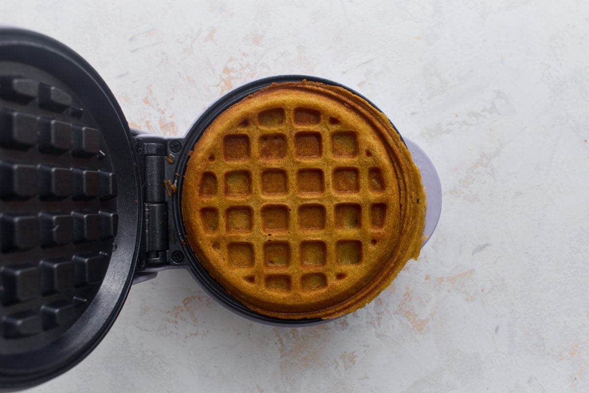 Golden brown oat flour waffle cooking in a waffle maker.