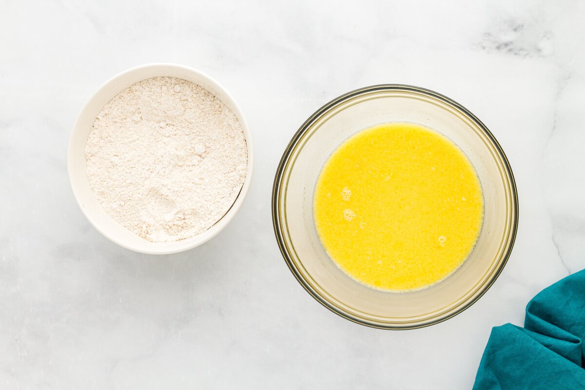 Wet ingredients for gluten-free vanilla cake donuts whisked together in a glass mixing bowl beside gluten-free flour.