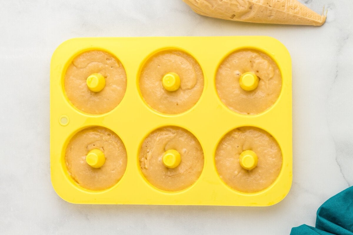 Gluten-free vanilla cake donut batter piped into a yellow donut pan before baking.
