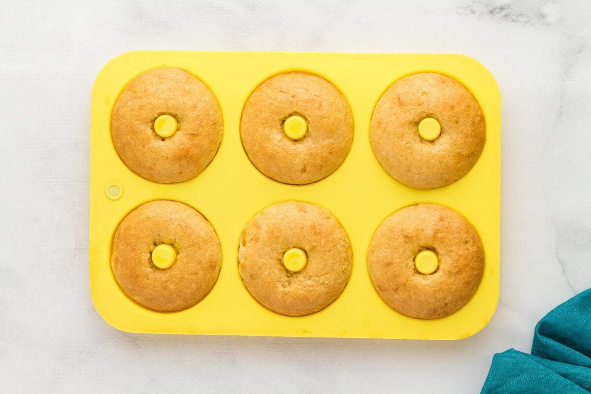 Freshly baked gluten-free vanilla cake donuts in a yellow donut pan with lightly golden tops.