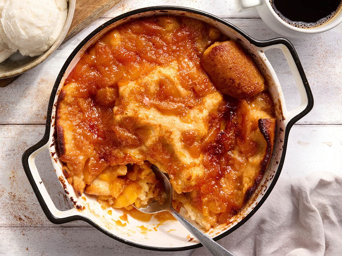 Gluten free peach cobbler scooped with a spoon showing the soft buttery topping and jammy peach filling underneath