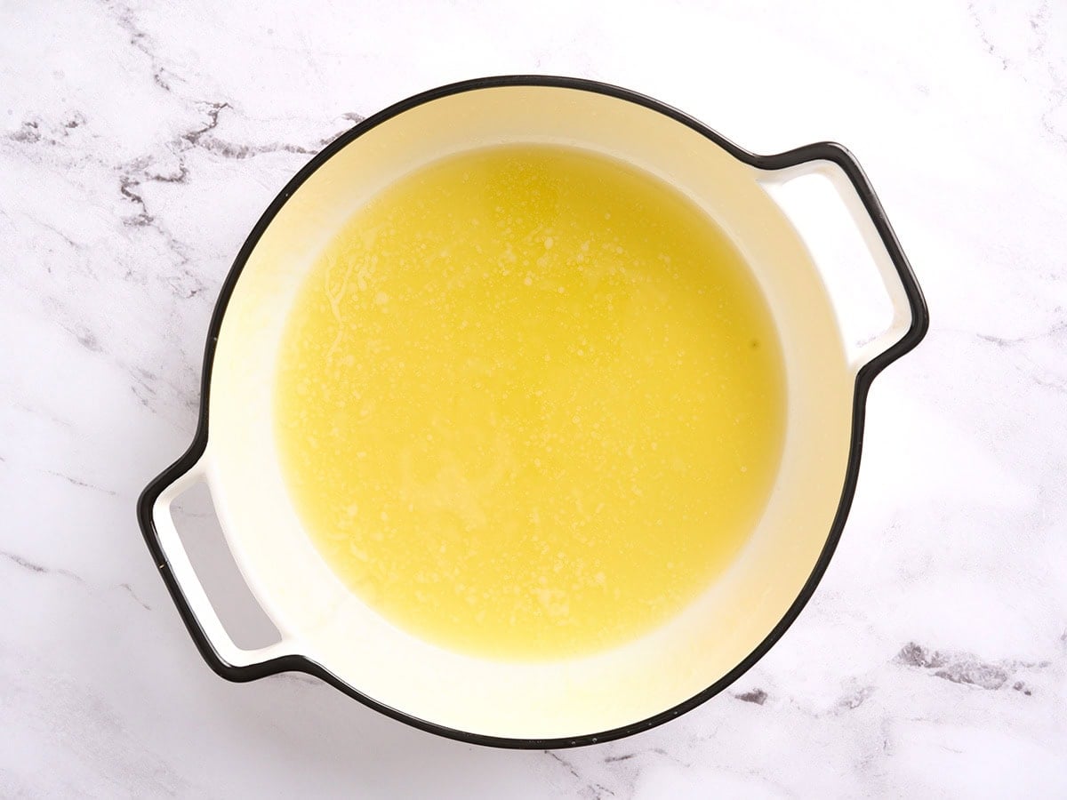 Melted butter poured into a white round baking dish to coat the bottom evenly