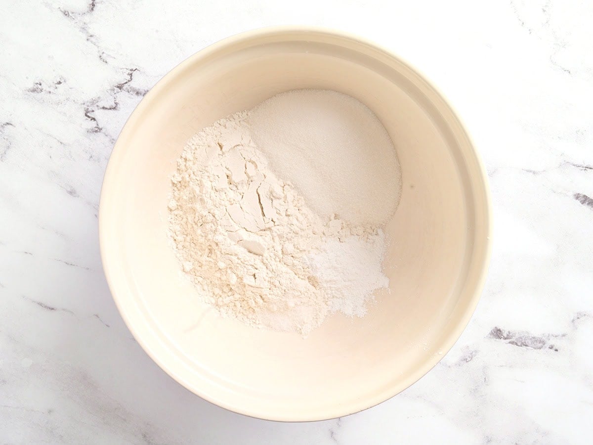 Gluten free flour, sugar, baking powder, and salt combined in a cream colored mixing bowl