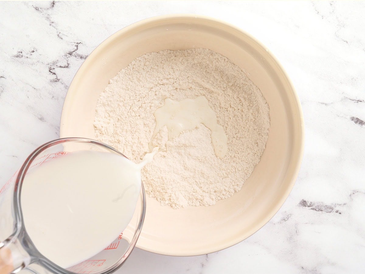 Milk being poured from a glass measuring cup into a bowl of gluten free dry ingredients
