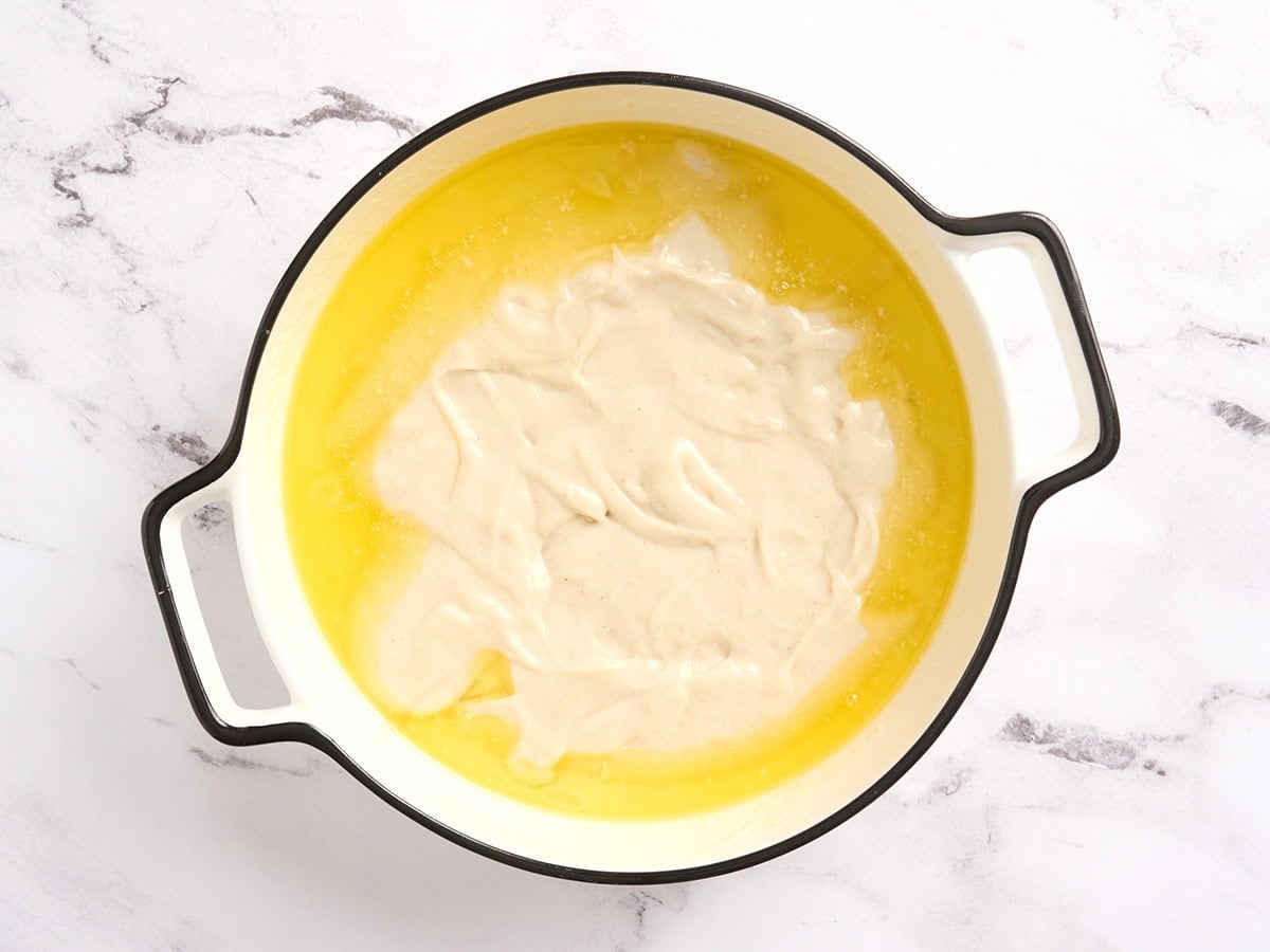 Thick gluten free cobbler batter poured over melted butter in a white round baking dish