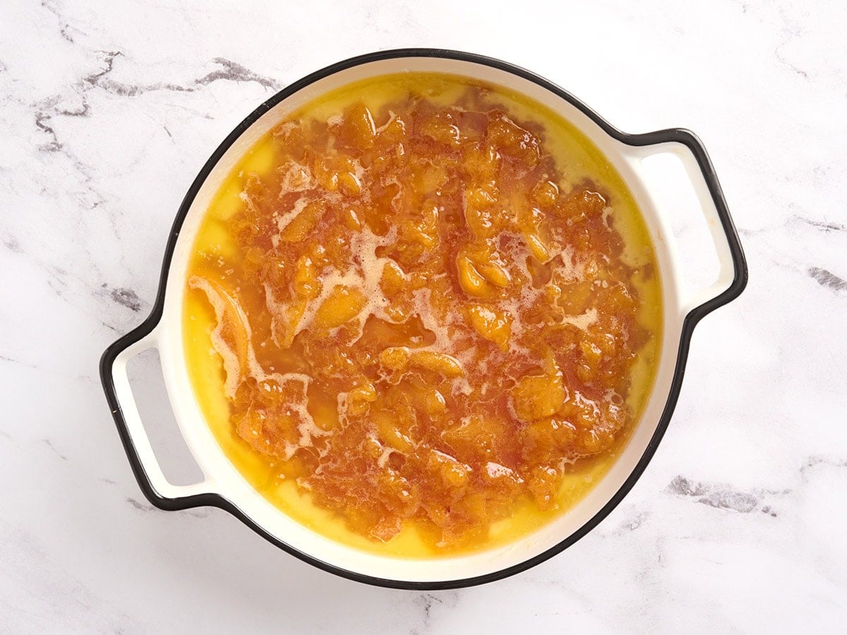Cooked peach filling and syrup spooned over the cobbler batter in a white round baking dish before baking