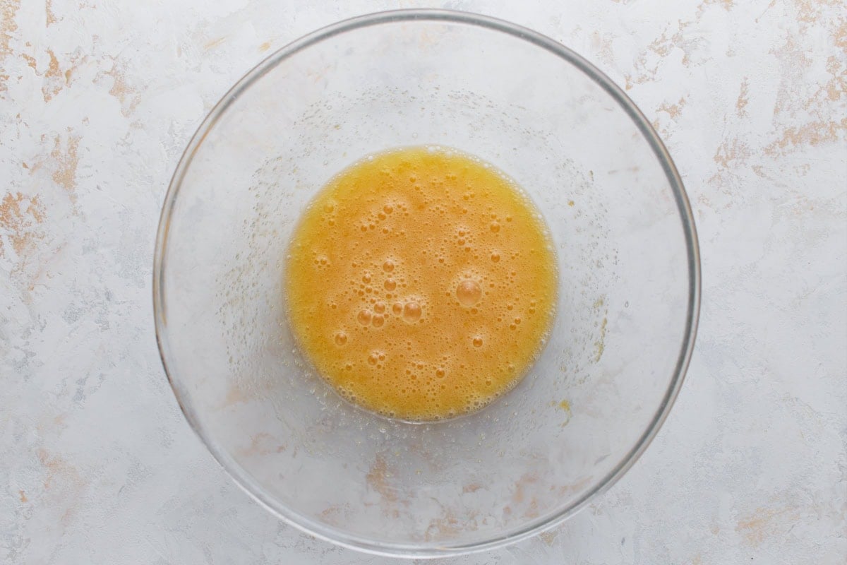 Overhead view of whisked eggs and oil in a glass mixing bowl
