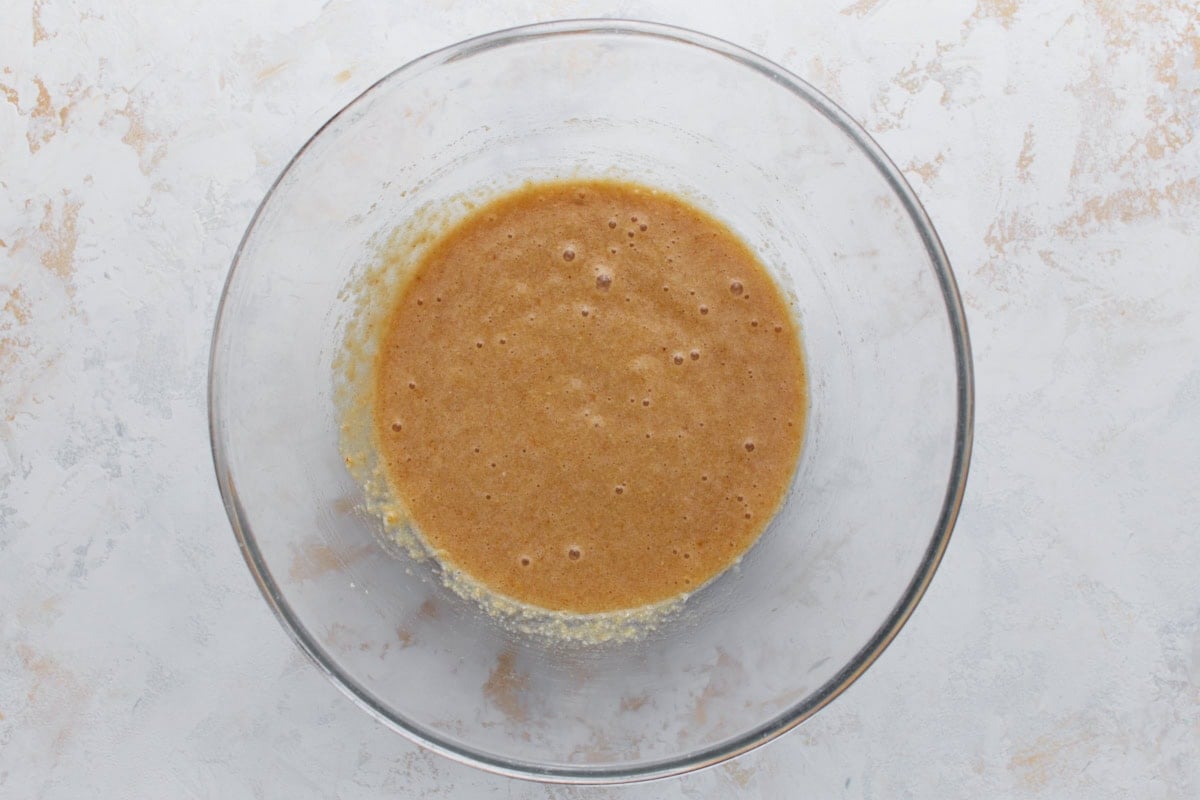 Overhead view of wet and dry ingredients combined into a smooth batter in a glass mixing bowl
