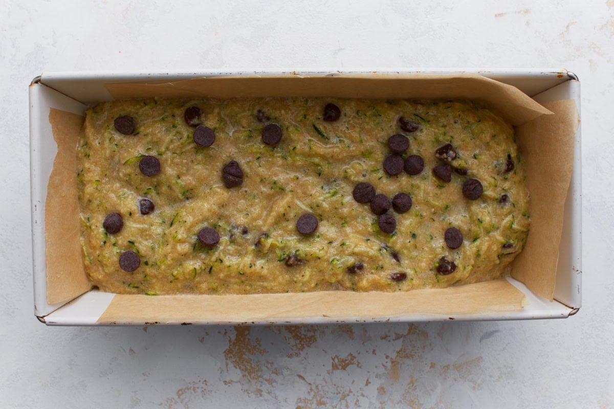 Almond flour zucchini bread batter with chocolate chips poured into a parchment lined loaf pan ready to bake