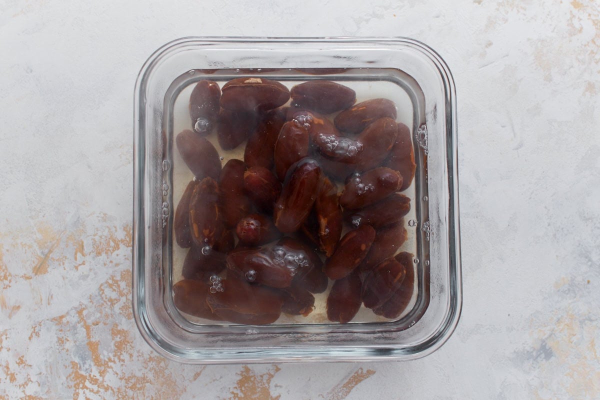 Pitted dates soaking in hot water in a glass container before blending for homemade date ice cream.