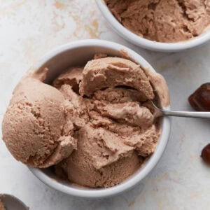 Date ice cream scooped into white bowls with a spoon, showing its creamy texture and caramel-colored appearance.