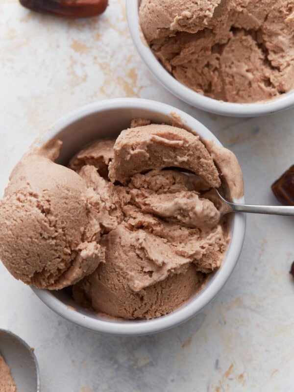 Date ice cream scooped into white bowls with a spoon, showing its creamy texture and caramel-colored appearance.