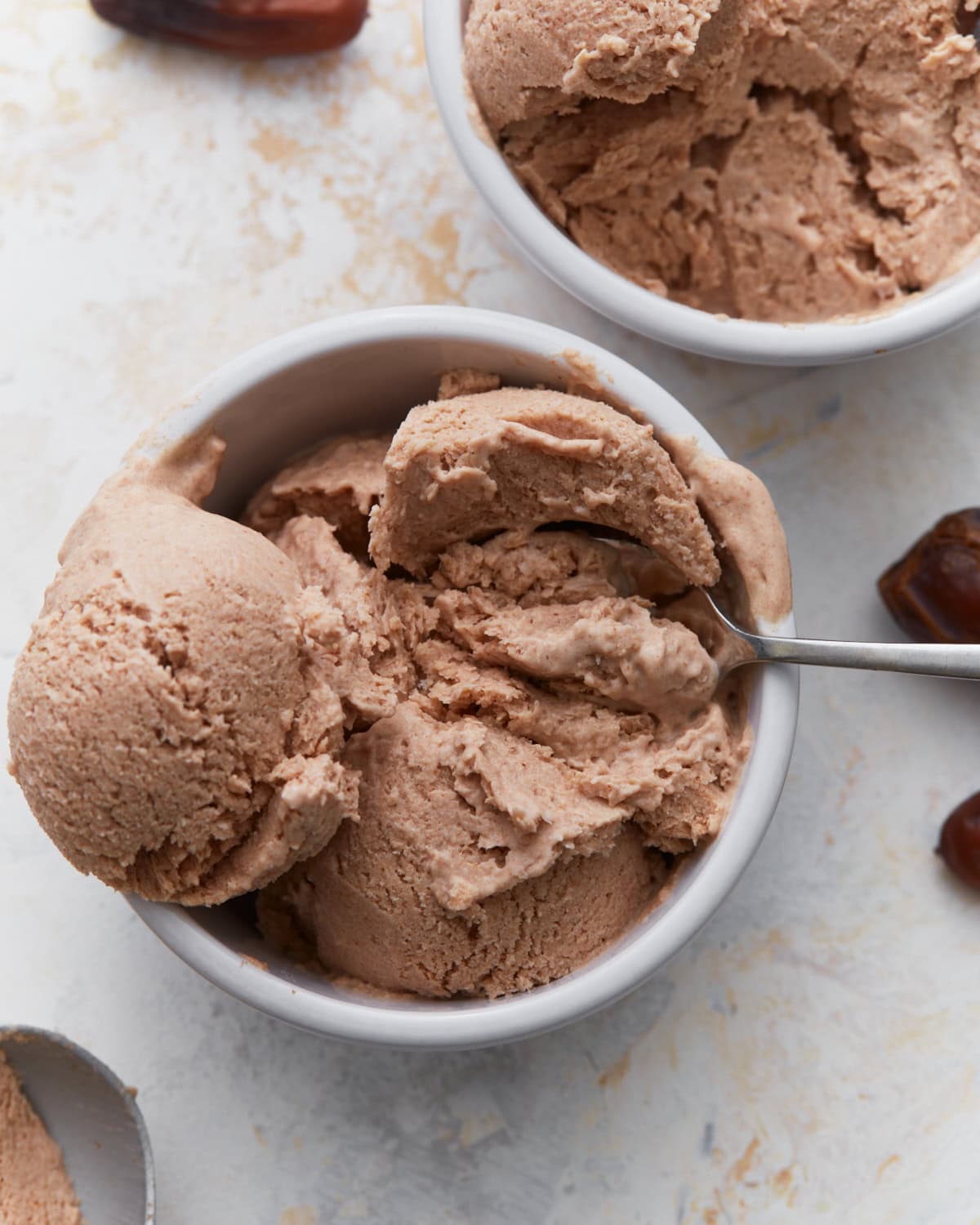 Date ice cream scooped into white bowls with a spoon, showing its creamy texture and caramel-colored appearance.