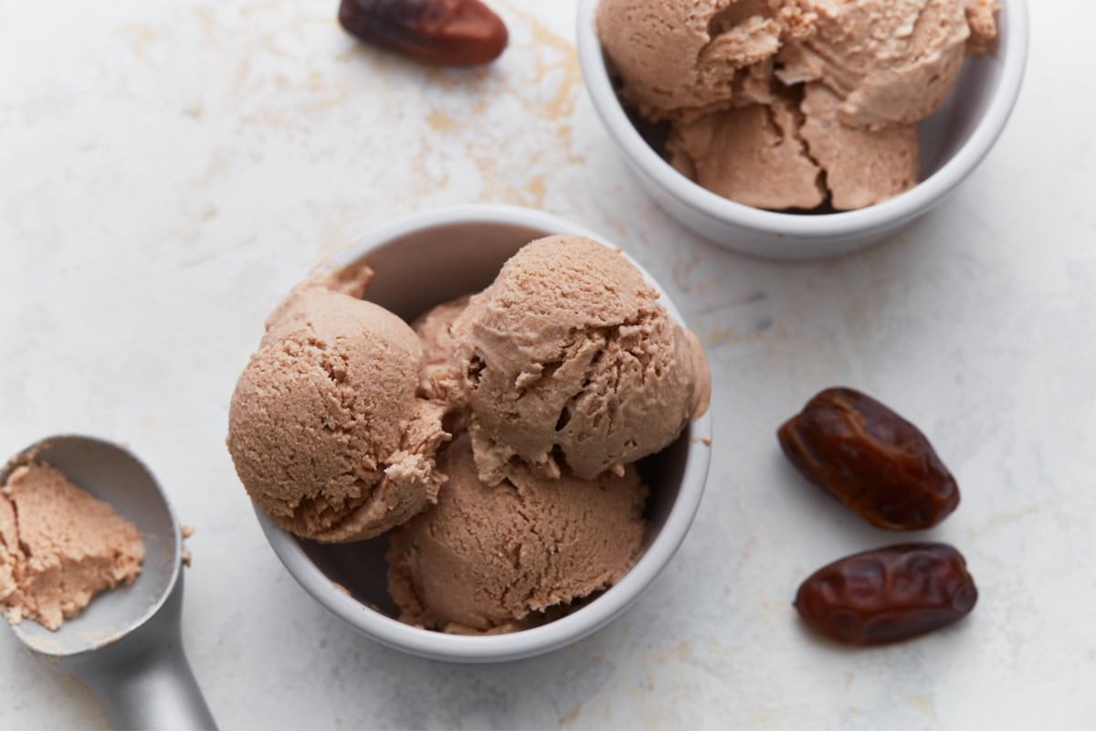 Three scoops of homemade date ice cream served in a white bowl with whole dates alongside.