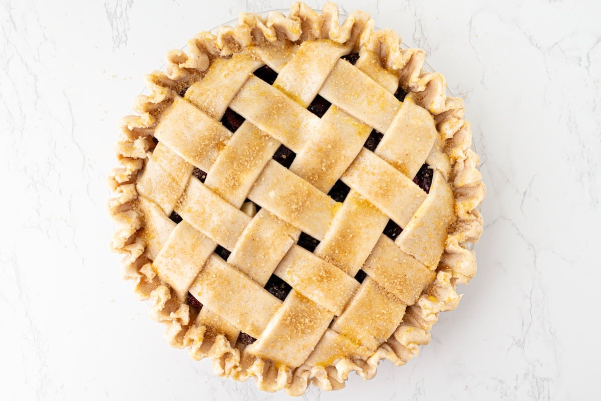 Overhead view of an assembled gluten-free cherry pie with a woven lattice top brushed with egg wash and sprinkled with turbinado sugar, with a crimped edge, ready to go into the oven.