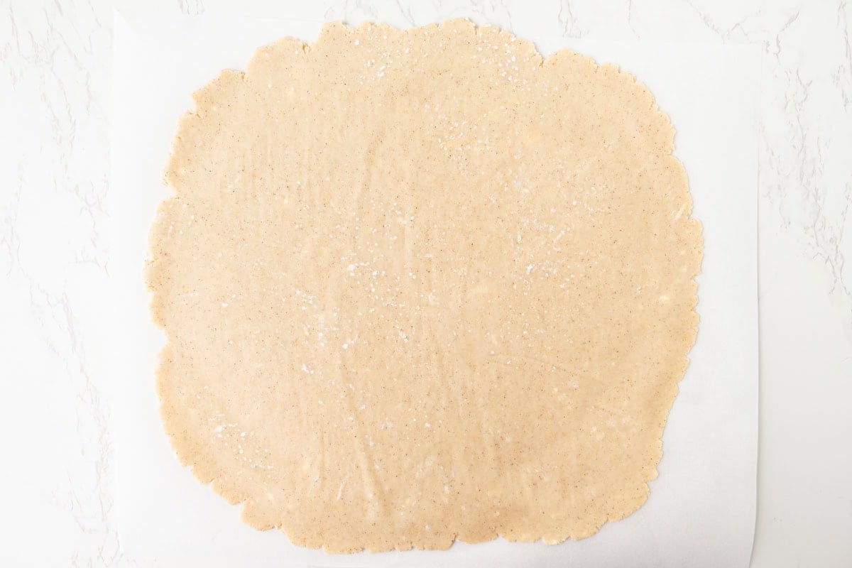 Overhead view of gluten-free pie crust dough rolled out into a thin 12-inch circle on a sheet of parchment paper on a white marble surface.
