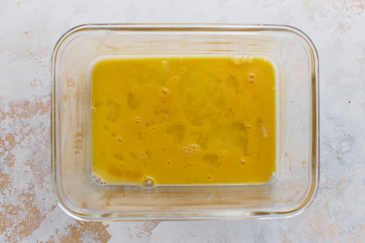 Beaten egg in a glass container prepared for coating the zucchini fries.