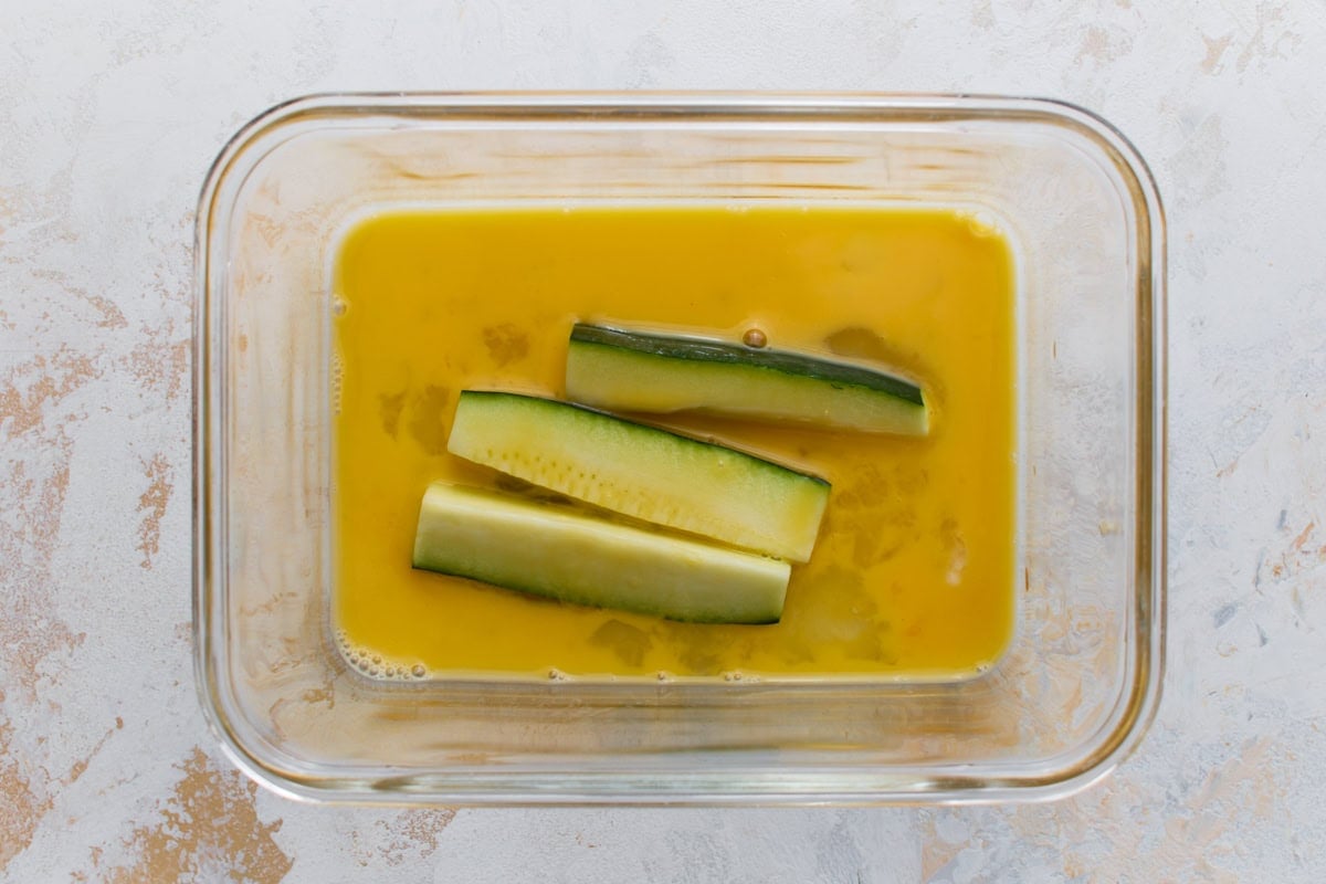 Zucchini sticks dipped in beaten egg before being coated in the Parmesan mixture.