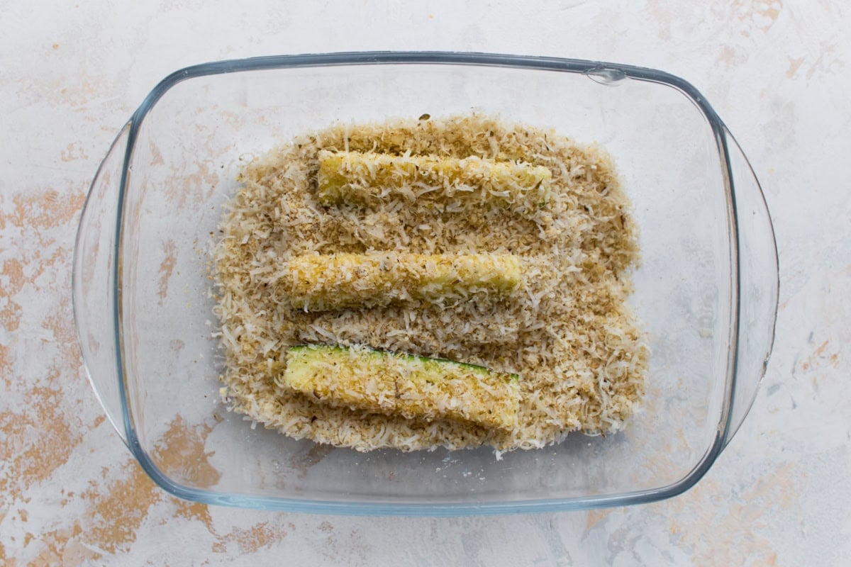 Zucchini fries coated in Parmesan and almond flour breading before baking.
