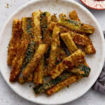 Crispy baked keto zucchini fries coated in Parmesan and almond flour served on a white plate with a side of ketchup.
