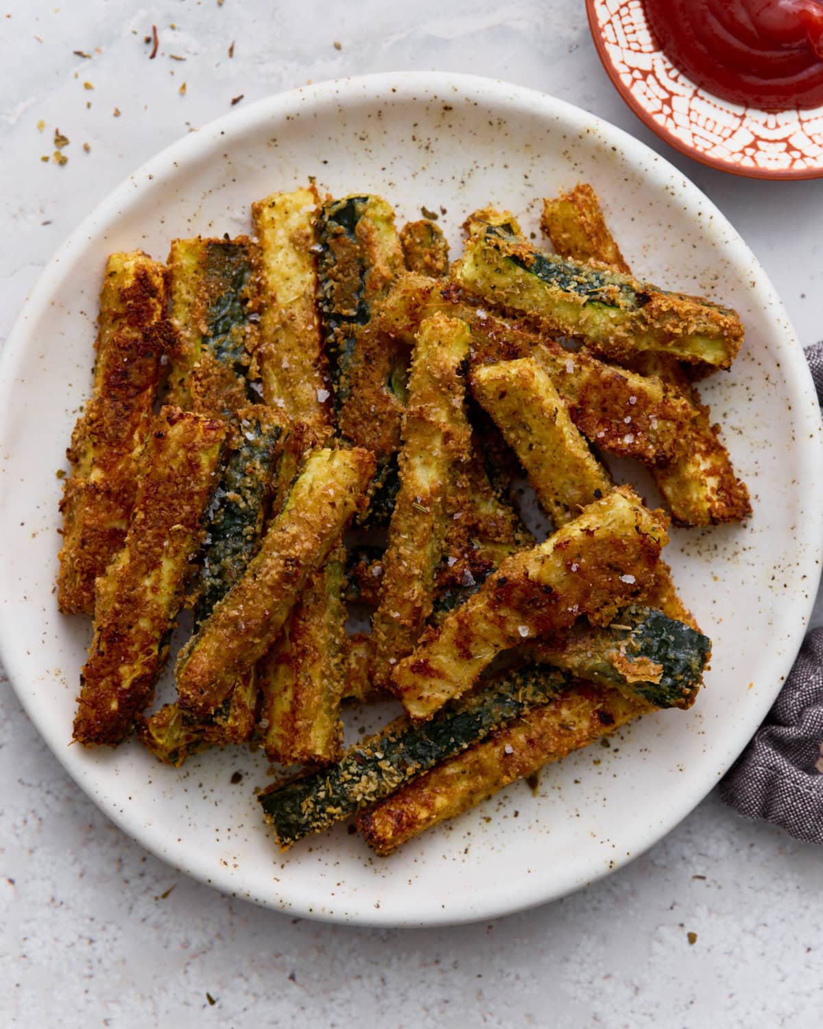 Crispy baked keto zucchini fries coated in Parmesan and almond flour served on a white plate with a side of ketchup.
