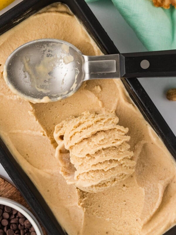 Overhead view of banana peanut butter nice cream being scooped from a black loaf pan with an ice cream scoop