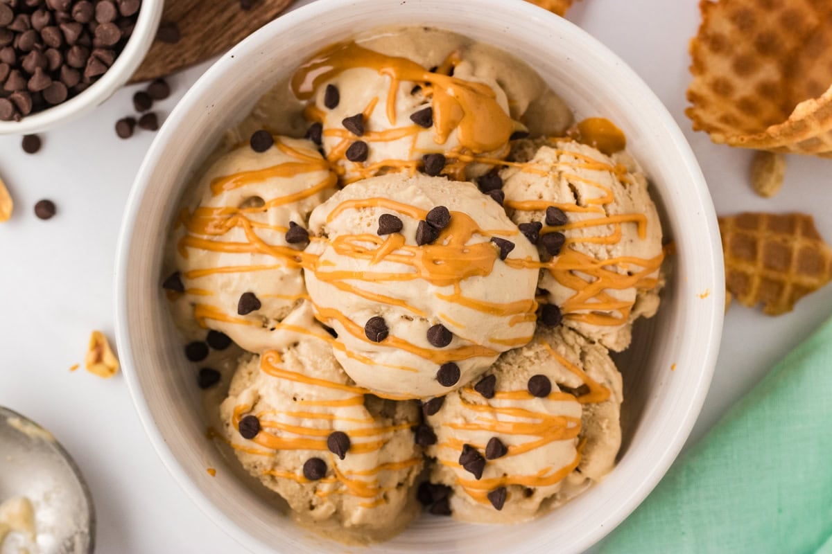 Overhead view of multiple scoops of banana peanut butter nice cream in a white bowl topped with mini chocolate chips and a melted peanut butter drizzle