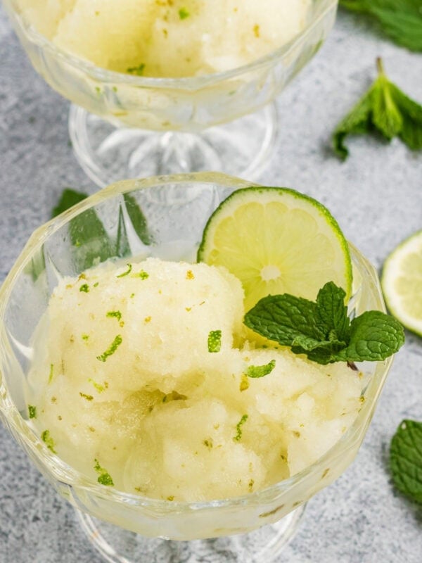 Lime sorbet scoops garnished with fresh mint and lime slices in glass dessert bowls.