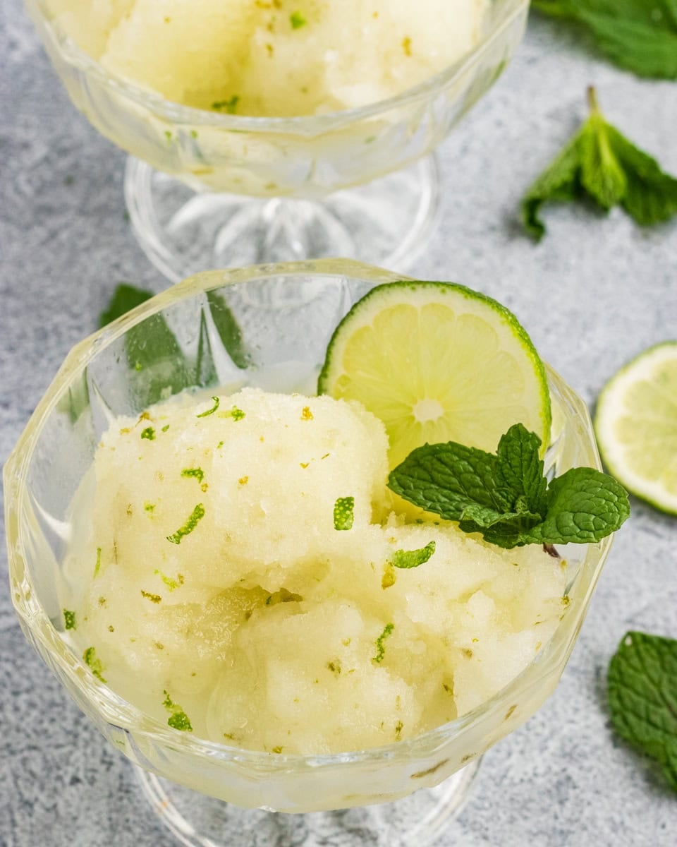 Lime sorbet scoops garnished with fresh mint and lime slices in glass dessert bowls.