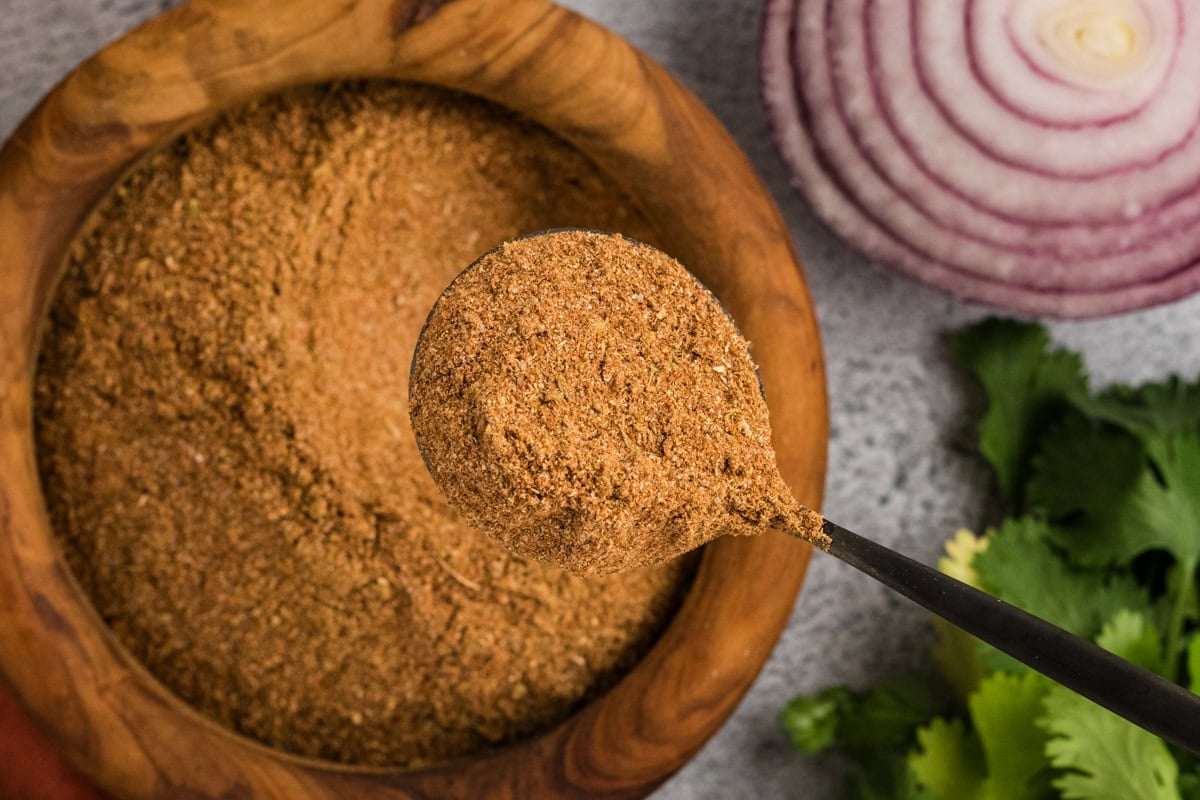 a spoon scooping homemade gluten-free taco seasoning from a wooden bowl