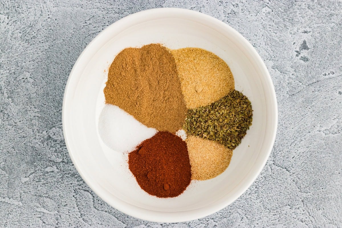 individual spices for homemade gluten-free taco seasoning measured into a white bowl before mixing