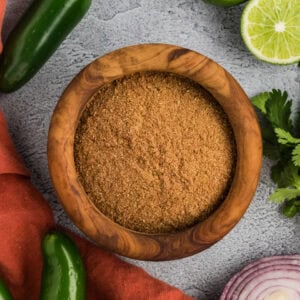 homemade gluten-free taco seasoning in a wooden bowl with jalapeños, lime, cilantro, and red onion