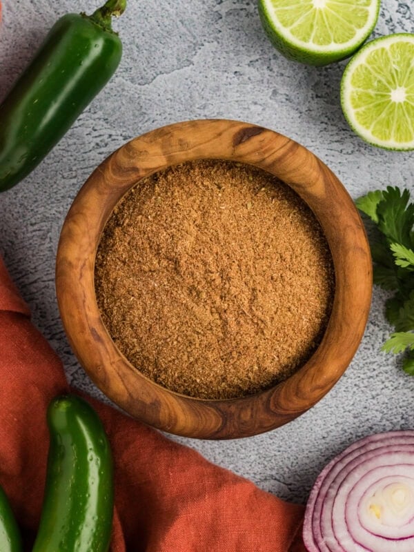 homemade gluten-free taco seasoning in a wooden bowl with jalapeños, lime, cilantro, and red onion