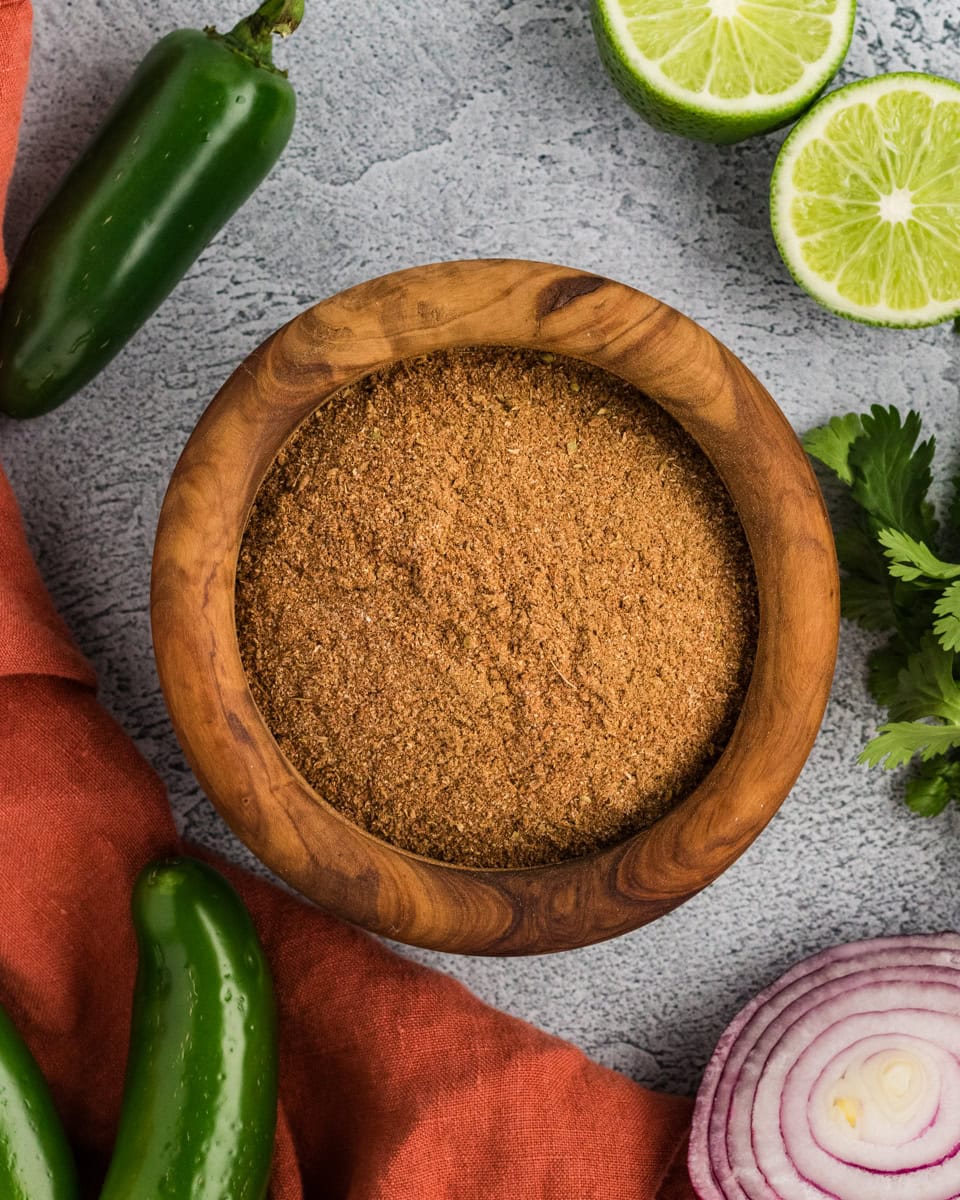 homemade gluten-free taco seasoning in a wooden bowl with jalapeños, lime, cilantro, and red onion