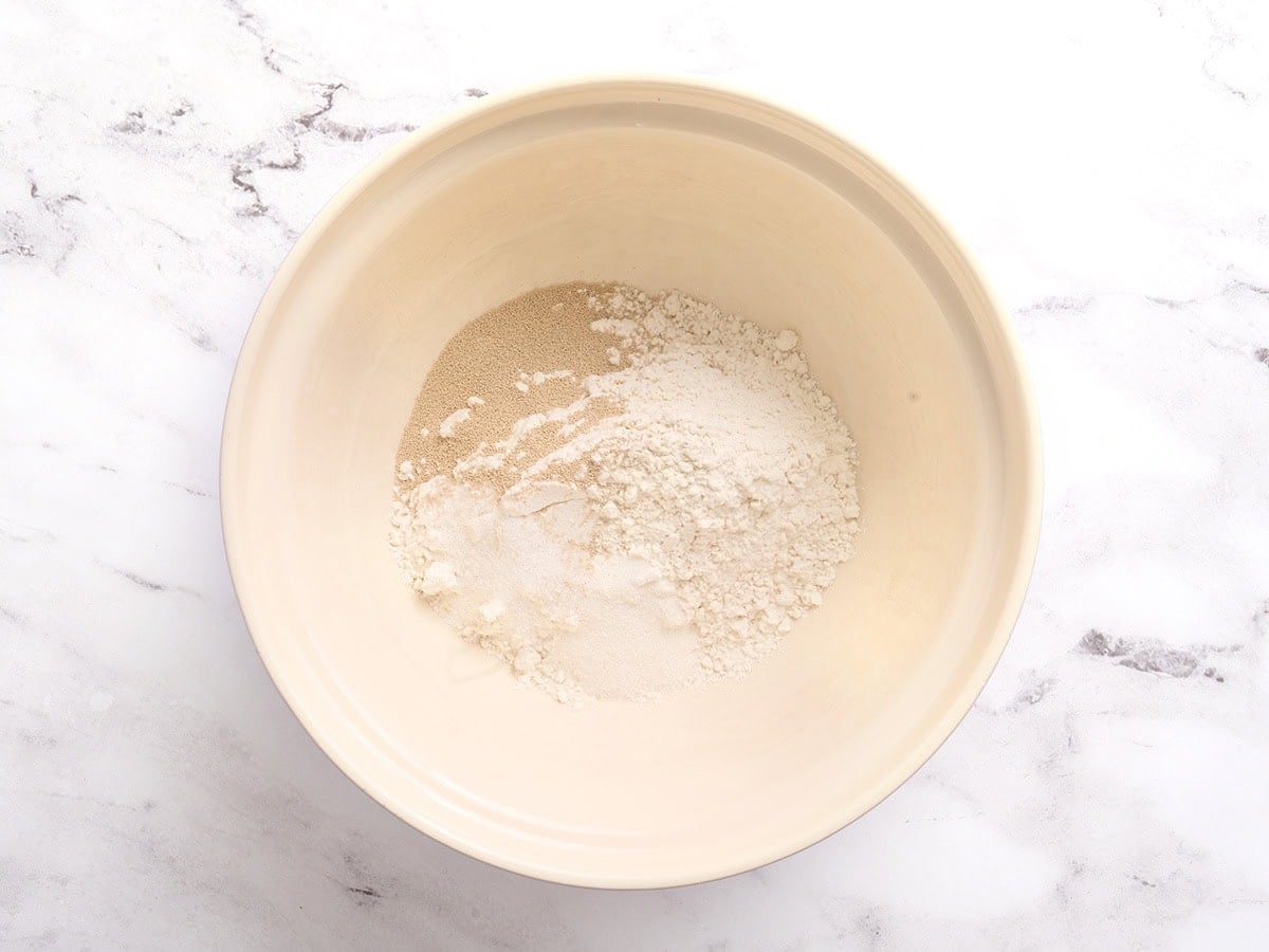Gluten-free bread flour, yeast, sugar, and salt in a mixing bowl before being whisked together.