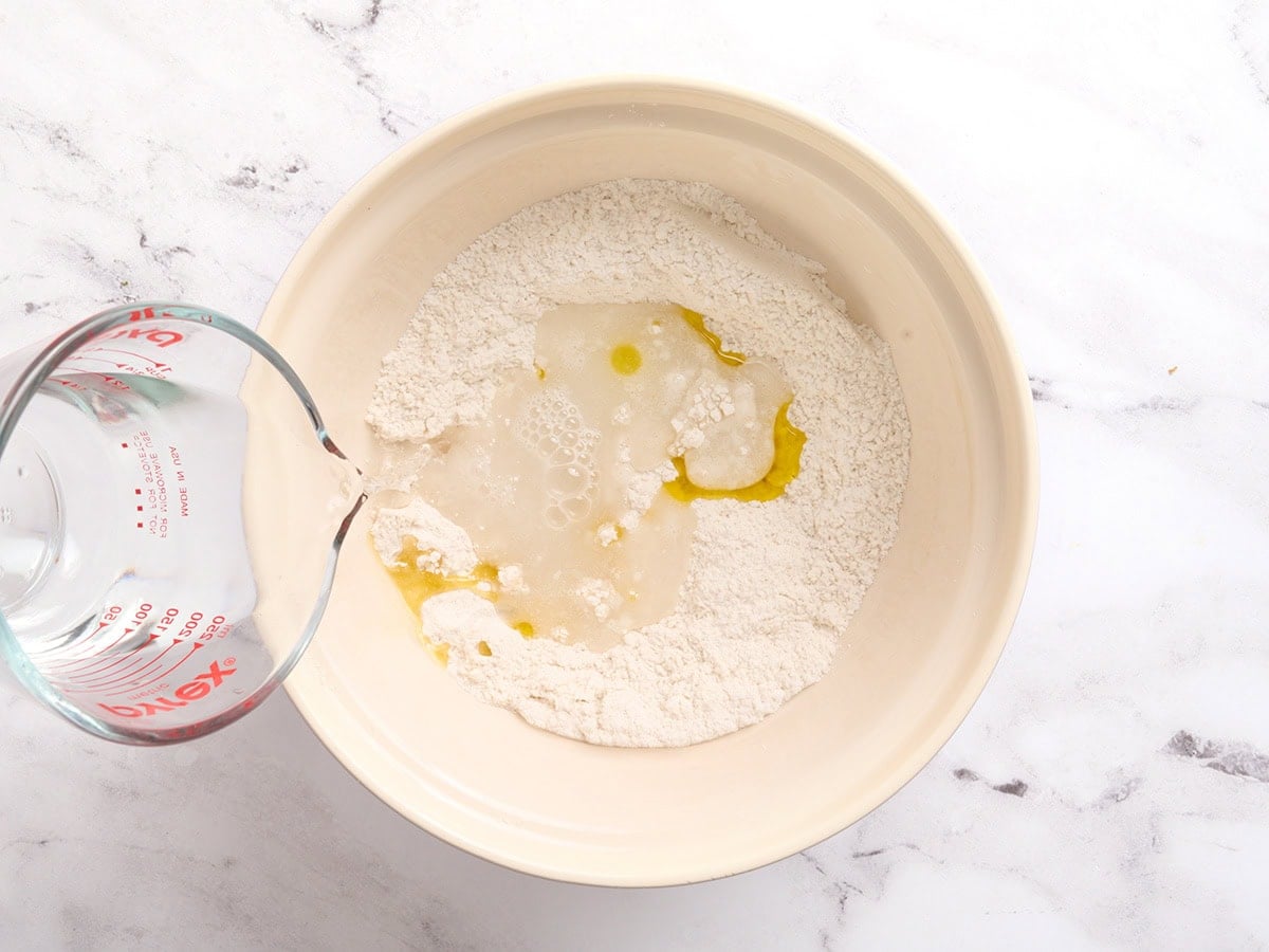 Warm water and olive oil being poured into gluten-free flour mixture to form pita dough.