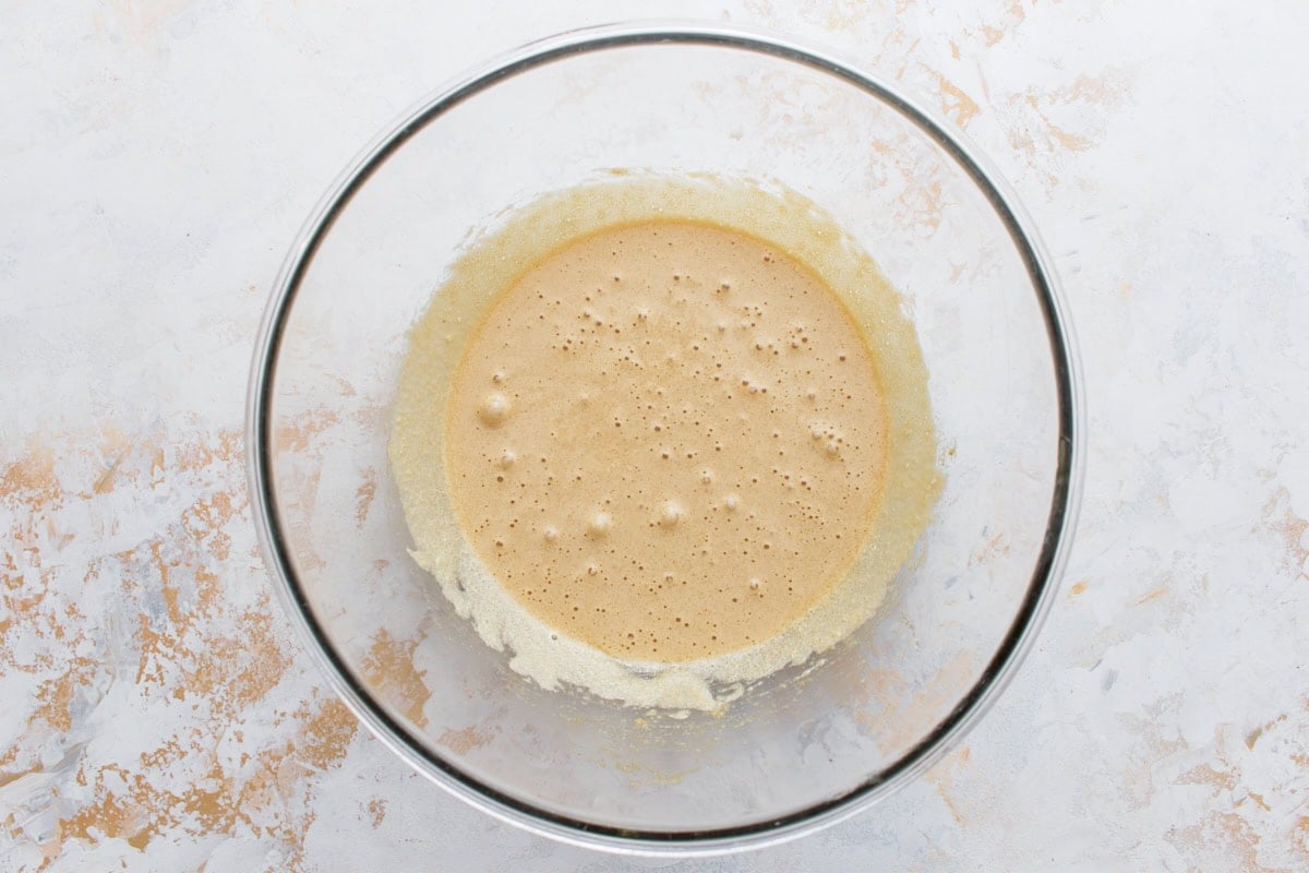 Eggs and sugar whisked until thick, pale, and bubbly in a glass mixing bowl.