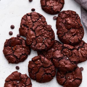 Overhead shot of flourless chocolate cookies stacked together, showing their shiny, crackled tops next to scattered chocolate chips.
