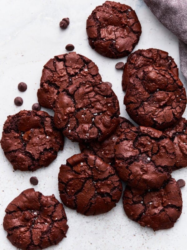 Overhead shot of flourless chocolate cookies stacked together, showing their shiny, crackled tops next to scattered chocolate chips.