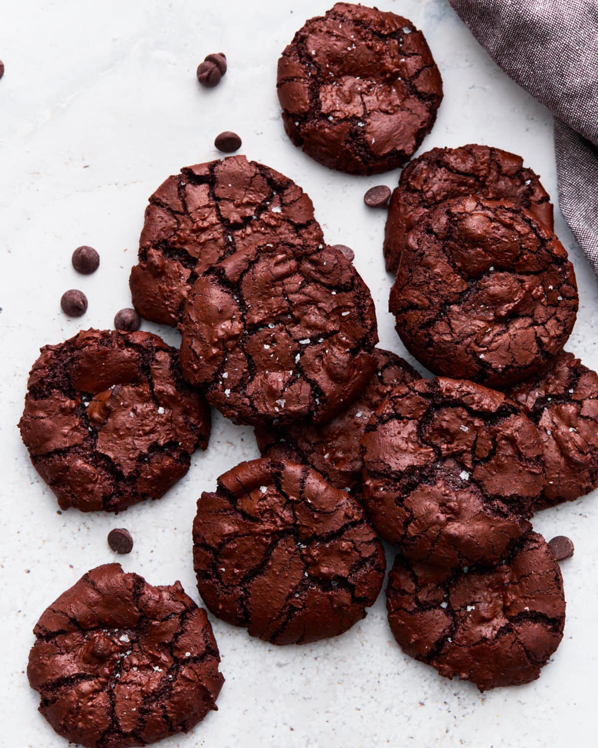 Overhead shot of flourless chocolate cookies stacked together, showing their shiny, crackled tops next to scattered chocolate chips.