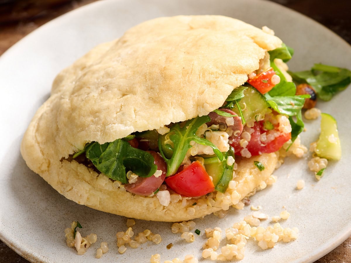 Gluten free pita bread stuffed with Greek quinoa salad, tomatoes, cucumber, and arugula.