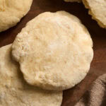 Overhead shot of shaped gluten free pita dough rounds resting on a wood cutting board before baking.