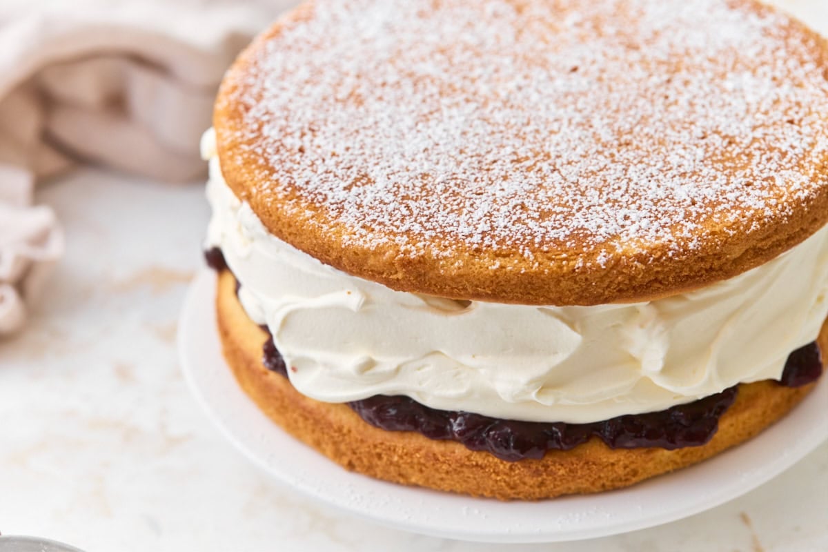 Assembled gluten-free Victoria sponge cake dusted with powdered sugar, with whipped cream and jam filling visible from the side