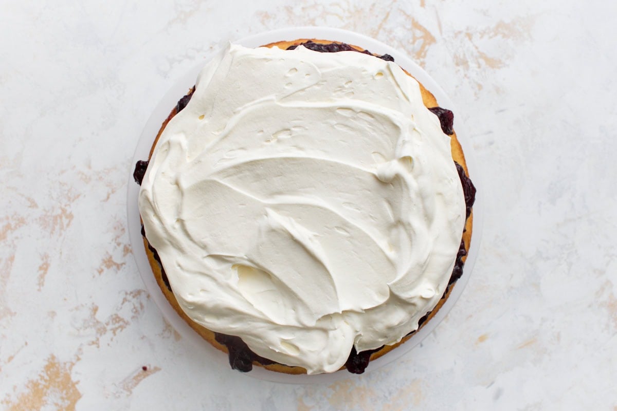 Whipped cream spread in swirls over the jam layer on the bottom sponge