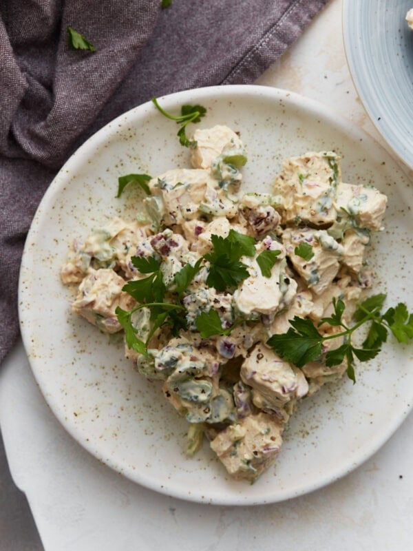 Keto chicken salad on a white plate garnished with fresh parsley, with a purple napkin and second plate in the background.