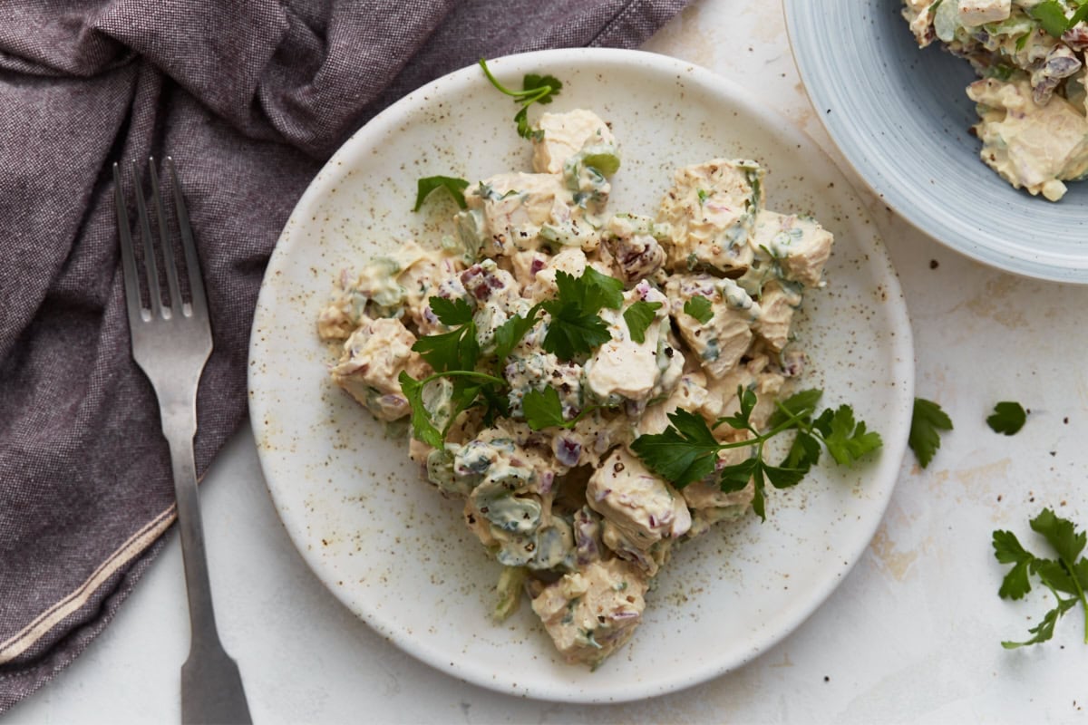 Keto chicken salad served on a white plate with fresh parsley, a fork, and a purple napkin, with a second bowl of salad in the background.