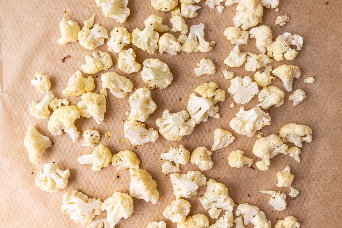 Roasted cauliflower florets spread on a parchment-lined sheet pan.