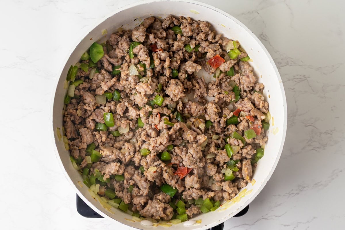 Ground Italian sausage cooked with onion, green pepper, and diced pepperoni in a skillet.